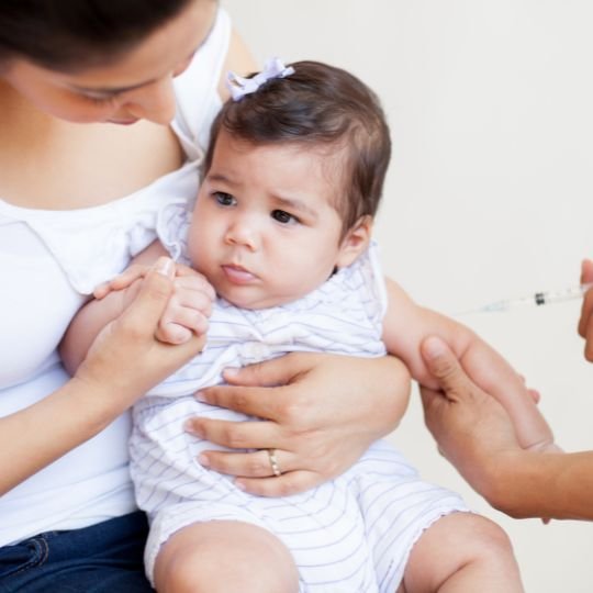 Baby getting a vaccination as her mother learns about fever after vaccines